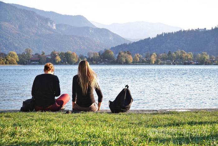 两个最好的朋友坐在美丽的湖和山背景前的草地上放松.玩得开心.