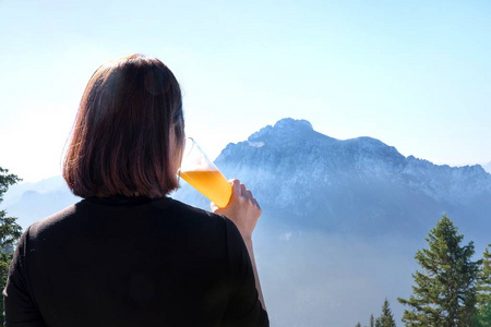 女人举起一杯啤酒，喝着生啤。在美丽的山景背景下，在户外享受收获的时光。喝啤酒。