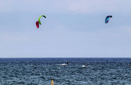 阿尔本加利古里亚意大利。 在阿尔本加海上的风筝冲浪，鲜艳的帆使蓝天活跃起来。 在水面上，木板的小径掠过帆。