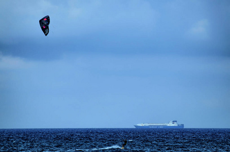 阿尔本加利古里亚意大利。 在阿尔本加海上的风筝冲浪，鲜艳的帆使蓝天活跃起来。 在水面上，木板的小径掠过帆。