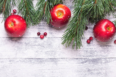 圣诞背景与树枝，红苹果和蔓越莓。 轻木桌。 降雪绘图效果。 上面的风景。 复制空间