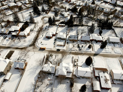 空中无人机查看道路和房屋冬季景观。 冬季城市街道从鸟瞰。 积雪覆盖建筑物的顶部透视图。 道路草坪，汽车和树木覆盖着上面的雪。