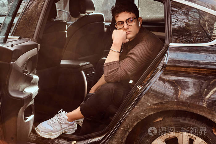 一个忧郁的年轻人戴着眼镜坐在豪华车的后座上.