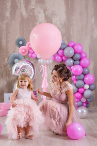 母亲和女儿一起庆祝家庭活动，两人都穿着粉红色的华丽礼服，头上戴着金色的皇冠。可爱家庭的工作室拍摄，柔和柔和的粉彩