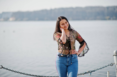 来自厄瓜多尔的漂亮拉丁模特女孩穿着牛仔裤，摆在湖边。