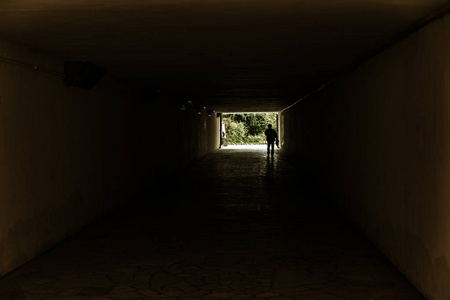 长长的石洞。在目的地的隧道尽头点亮..隧道中的剪影在道路尽头的光线背景下。令人毛骨悚然的图片作为设计的背景。