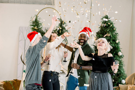 一群快乐的时尚打扮的朋友站在圣诞装饰前，庆祝新年，喝香槟