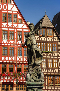德国法兰克福市中心的一座法官女雕像，上面有鳞片和剑，上面有古老的传统木制建筑