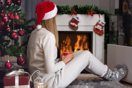 女孩头上戴着红帽子和睡衣. 女孩在火上取暖,拿着一杯茶.