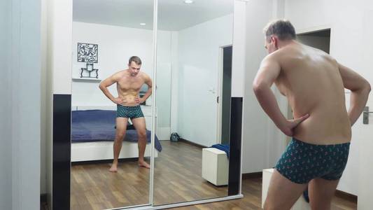 年轻人在卧室的镜子前检查他的肌肉