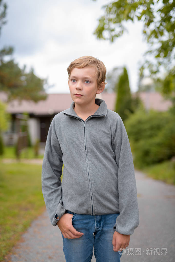 年轻的金发碧眼的英俊男孩思考, 而站在户外