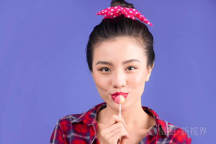 在蓝色背景下吃棒棒糖的迷人女孩