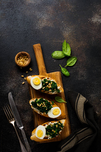 煎菠菜鸡蛋和松子三明治在棕色老式混凝土背景上。 美味健康的早餐或小吃。 上面的风景。