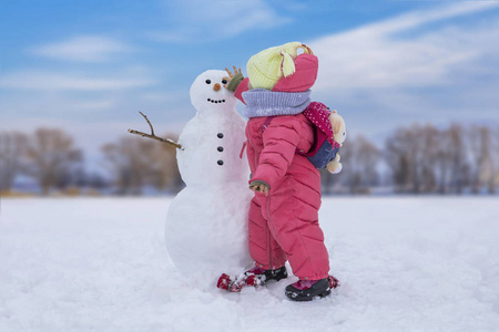 可爱的小女孩在雪亮的地方堆雪人。 冬季户外活动