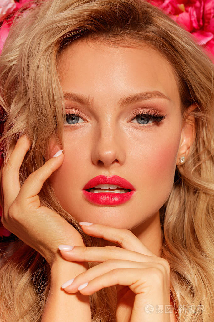 美丽的金发时尚模特的肖像蓝色的眼睛和红色的嘴唇在花的背景概念婚礼