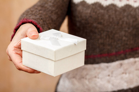 女人手里拿着一个白色的礼盒。 浅场深选择性聚焦在盒子上。 节日或生日礼物的概念。