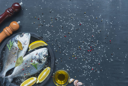 黑桌上有盐和胡椒覆盖的原料鱼的顶部视图