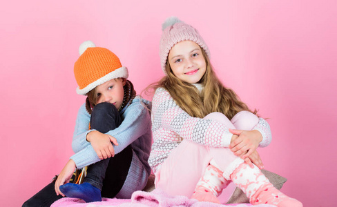 保持温暖和舒适。温暖你的冬季穿着与可爱和舒适的配件。兄弟姐妹戴着冬天温暖的帽子, 坐在粉红色的背景上。孩子们和女孩用毛衣和帽子热
