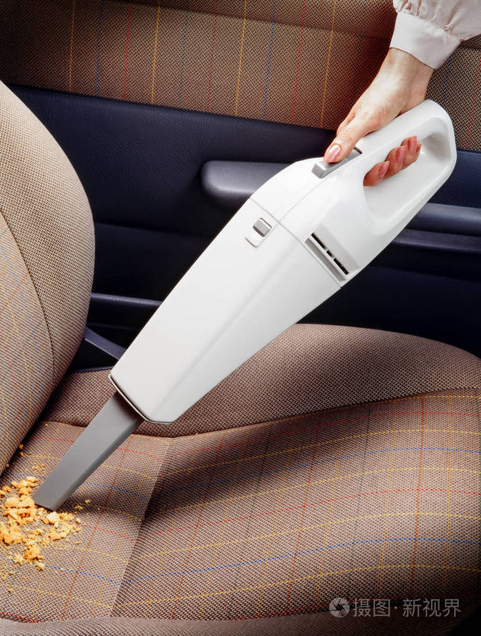 用便携式吸尘器清洁汽车内饰的女士手