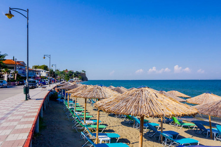 公共海滩上方的人行道上涂满了遮阳伞和甲板椅，游客放在海岸线旁边。