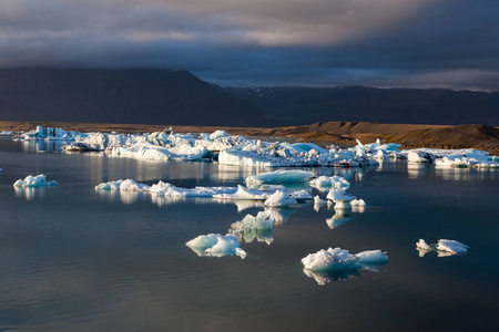 在 Jokulsarlon 冰川泻湖海岸附近分散融化的冰山上的多云日落全球变暖