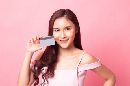 年轻的亚洲女人指着粉红色背景上的空白卡片