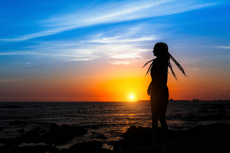 在令人惊叹的日落中，年轻女子在海上海岸的剪影。
