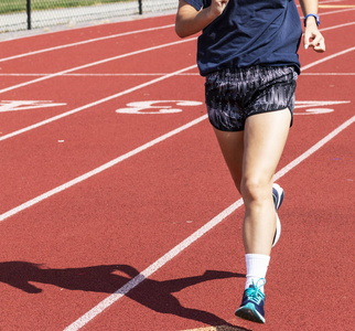 阳光影子一位高中跑步者正在一个阳光明媚的日子里跑在红色的跑道上