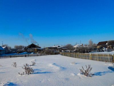 一个冬天晴朗的一天，一个乡村景观，一个覆盖着雪的乡村花园。 冻结的树枝。 在背景中可以看到小房子。