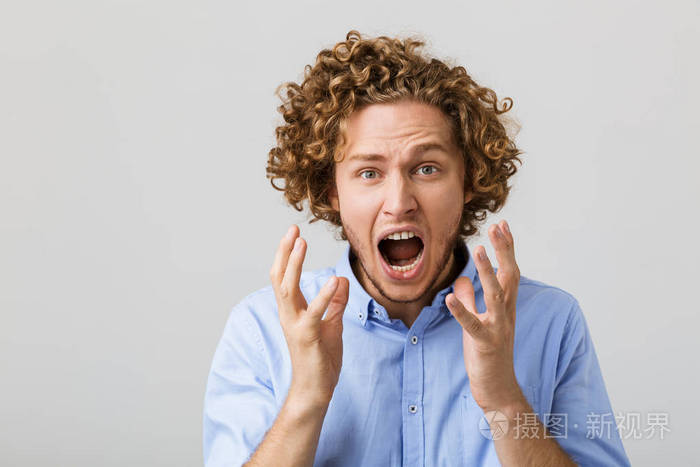 一个震惊的年轻人穿着衬衫站在灰色背景下尖叫着