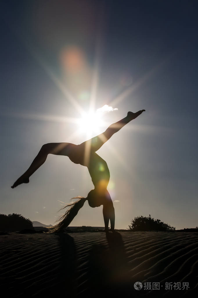 女性剪影做倒立瑜伽姿势海滩在明亮的背部照明