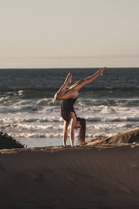 在沙岸的瑜伽倒立中坚强的女人的侧视，背景是海浪