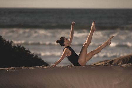 年轻优雅的女人坐在沙滩上，在背景上和平地做瑜伽体式