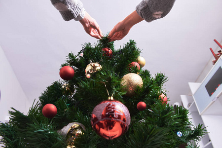 穿毛衣的年轻女子用球装饰圣诞树的底部景色。新年和圣诞节。假日概念。