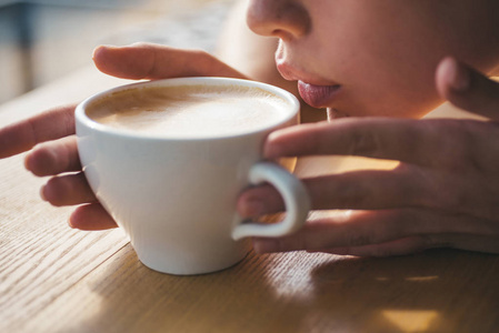 在咖啡厅或商店放松身心, 喝酒。新鲜的早晨咖啡与牛奶和奶油泡沫。完美的早晨最好的咖啡。女孩闻到香气咖啡杯。味道很好。新鲜咖啡