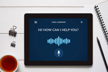 语音助理概念在平板电脑屏幕上与办公室物体在白色木桌上。所有屏幕内容由我设计。平躺式