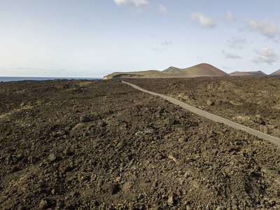 西班牙加那利群岛兰萨罗特岛的浮雕火山和熔岩场的空中景观。崎岖的海岸线和沿着大海行驶的道路