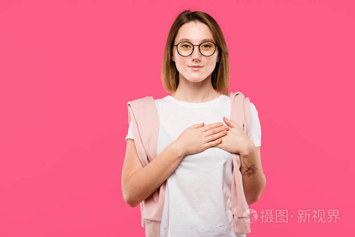 戴眼镜的时髦女孩,双手握在胸前,与粉红色隔离