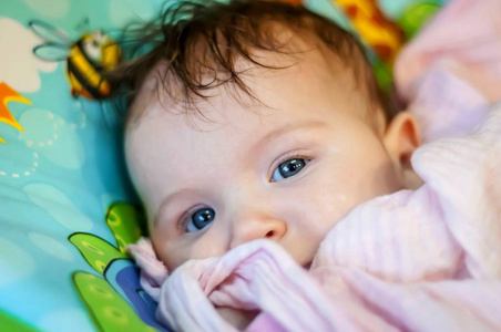 可爱健康的微笑，温和快乐，积极的新生婴儿白种人女婴，深蓝色的眼睛好奇地从她的床上偷看。 健康的婴儿儿童概念。