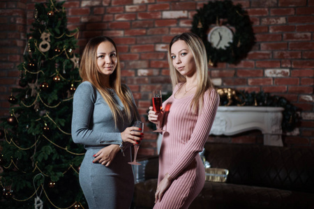 两个年轻漂亮的女朋友或姐妹在家一起庆祝圣诞节，手里拿着香槟
