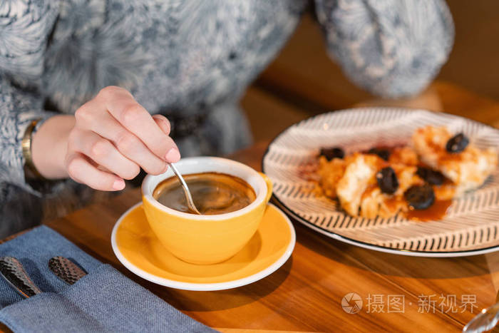喝咖啡的年轻女子女子拿着杯子坐在木桌的咖啡店里在桌上加早餐愉快的