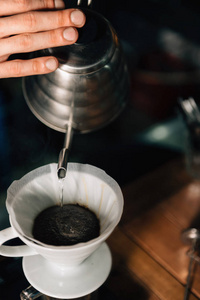 关闭咖啡师从水壶倒开水到陶瓷滴咖啡机的垂直图像。