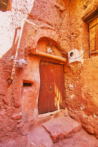 旧的木制弯曲的门在中世纪房子的角落，覆盖着红色的赭石泥，伊朗。