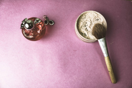 美容盒, 易碎的哑光矿物粉末与一个特殊的天然棕色木刷从自然午睡化妆, 粉红色的香水和闪亮的银色耳环在粉红色的紫色背景。平躺着。顶