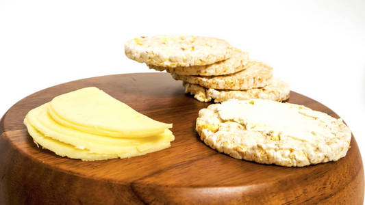 一套白色背景的保健食品。 白色背景上分离的膨化米面包。 侧视木制桌子和奶酪片与刀。 特写香脆的膳食荞麦健身面包