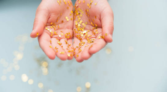 s hands with golden confetti stars on blue background.