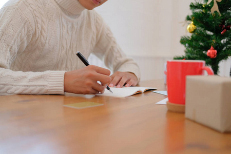 在圣诞节新年庆祝活动中，男人穿着奶油毛衣，在笔记本上写纸条。