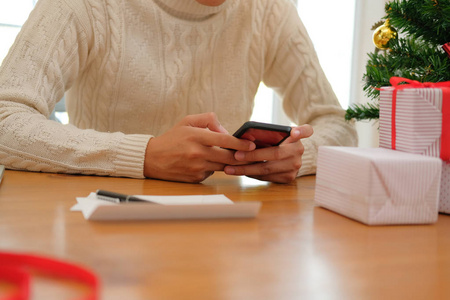 男人穿着奶油毛衣，用手机智能手机装饰圣诞。 圣诞节新年假期庆祝活动。
