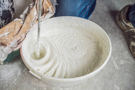 男油漆工用手持搅拌机在桶内揉腻子.照片