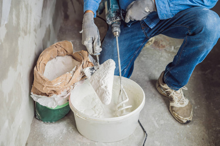 手持搅拌机男油漆工用手持搅拌机在桶内揉腻子.照片